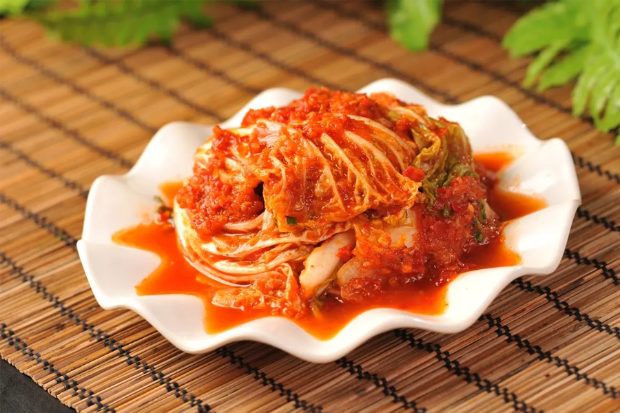 泡菜（Kimchi），韩国传统发酵食品，展示泡菜鲜艳的橙红色，呈现在竹制餐垫上。泡菜作为韩国饮食文化的代表性食物之一，也是牛津词典中收录的第一个韩文单词。