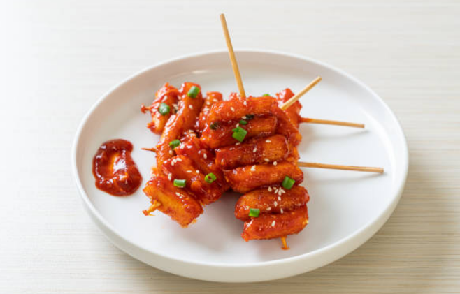 Plato de tteokbokki, un popular aperitivo coreano hecho de pastel de arroz, servido con salsa picante y adornado con cebollines.