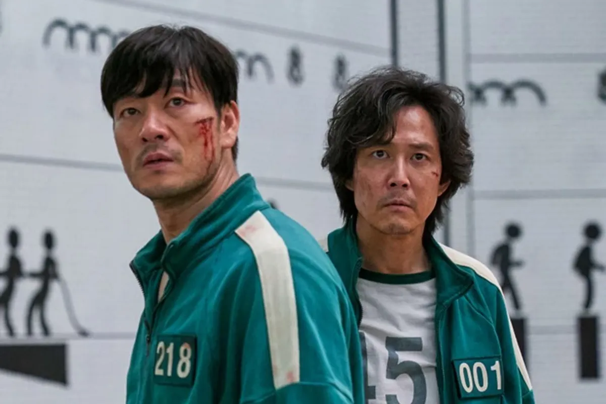 穿著綠色運動服的《魷魚遊戲》參賽者站在牆壁前，背景顯示比賽中使用的道具，出自Netflix影集場景。