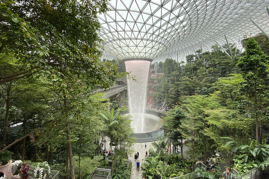 新加坡樟宜机场内部景观，展示了多层次的绿色植物和中央瀑布，象征着现代与自然的完美结合。