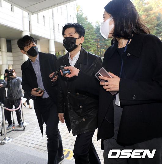 裁判所外で報道陣に囲まれる黒いジャケットを着た男性