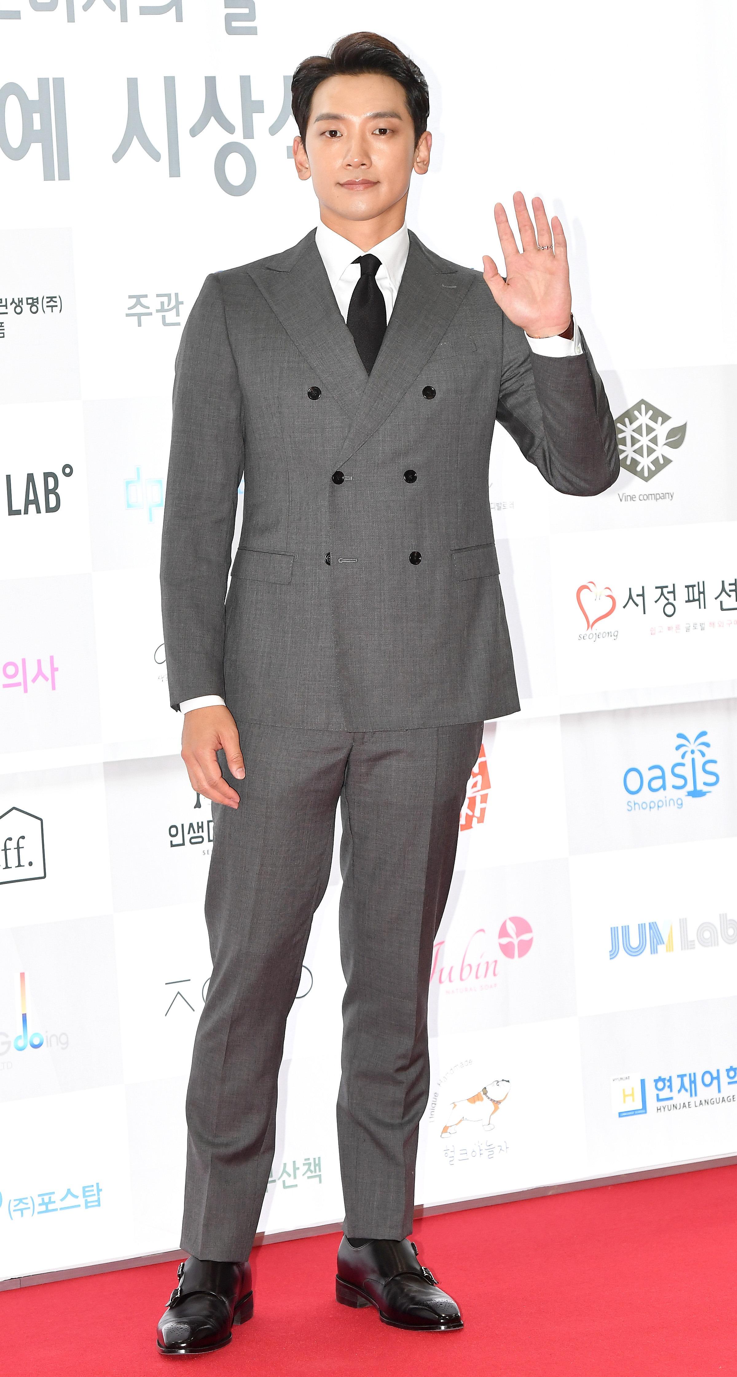 俳優の赤いカーペットでのスーツ姿、片手を上げている様子