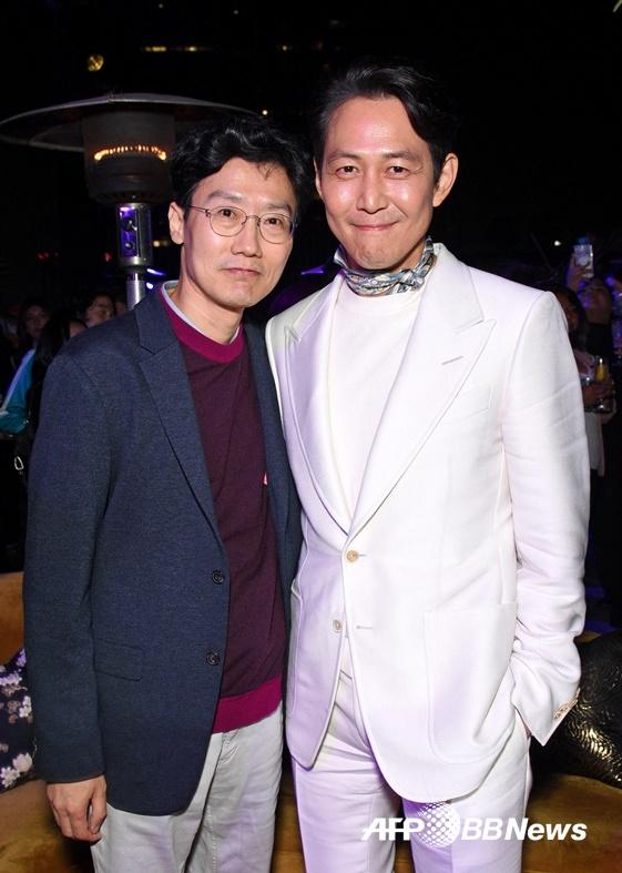 Netflixのイベントで並ぶ白いスーツ姿のイ・ジョンジェと黒いスーツ姿の人物、華やかな背景で記念撮影