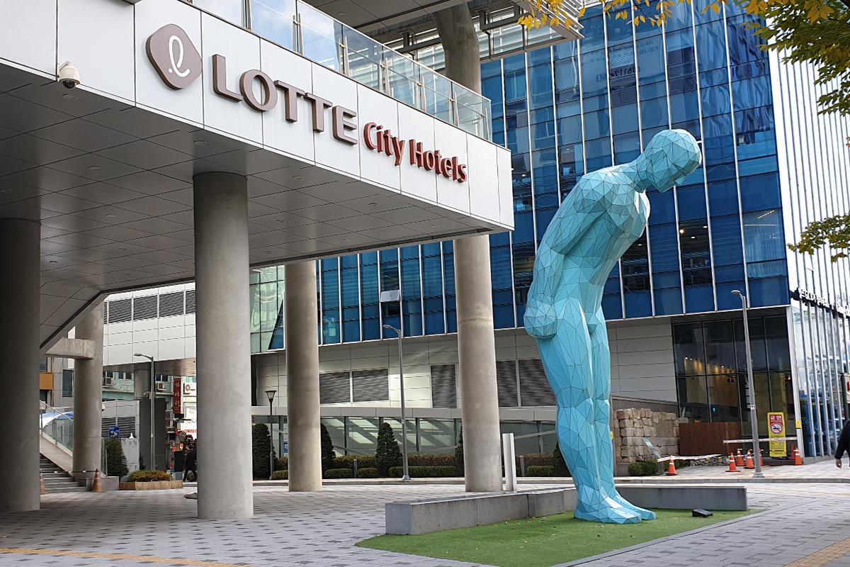 View of Lotte City Hotel Myeongdong entrance with modern sculpture in front, capturing the architecture's sleek design in vibrant hues.