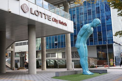 The front entrance of Lotte City Hotel Myeongdong with a blue statue bowing in front. 