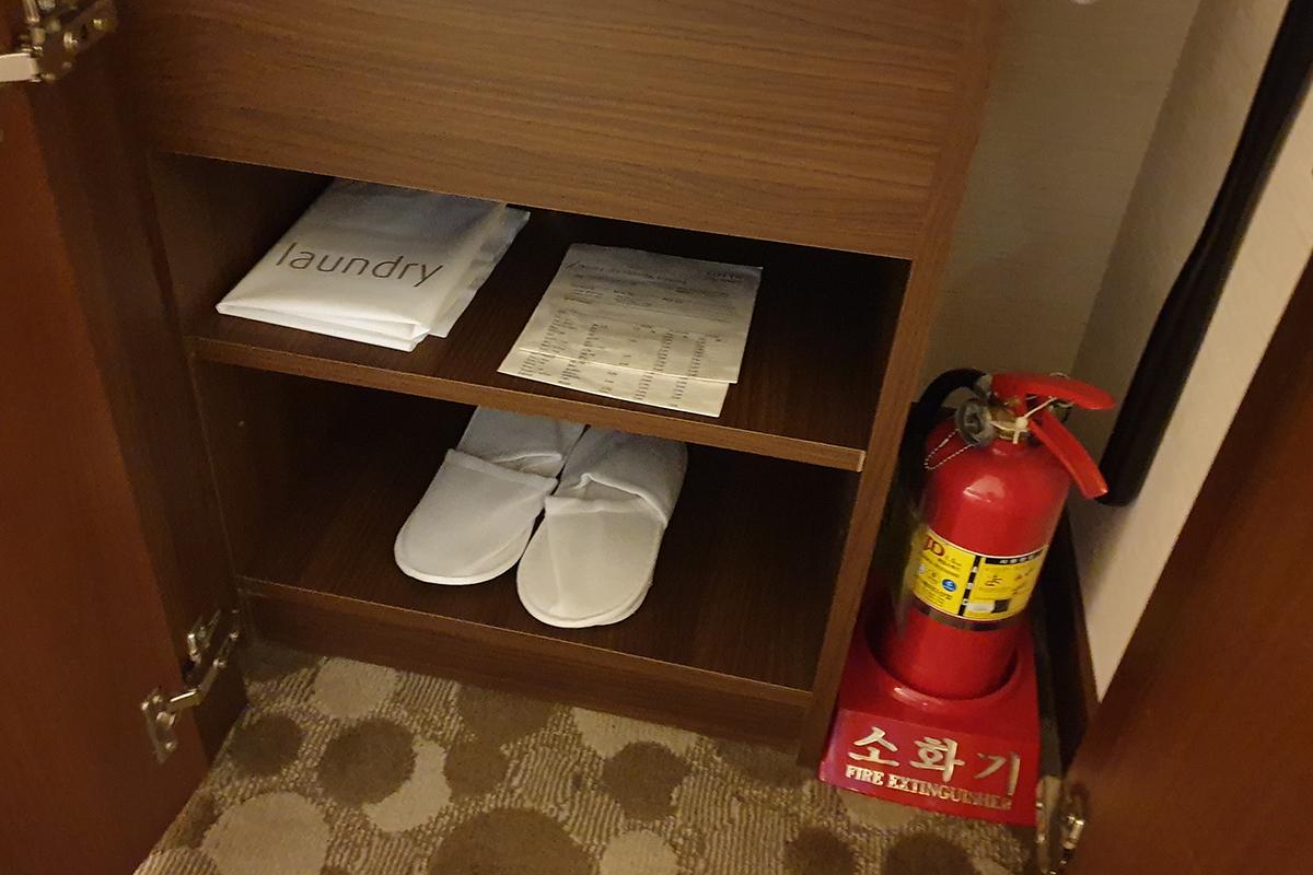 In a cabinet, there is bags for laundry and slippers. Next to the cabinet is a fire extinguisher.
