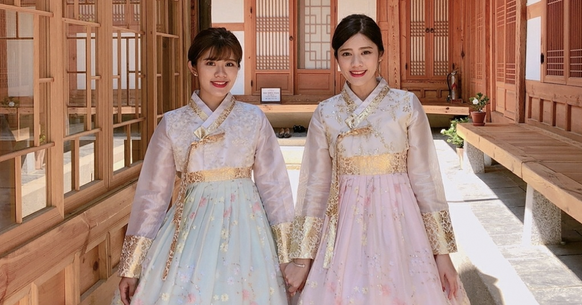 Hai người mặc hanbok truyền thống Hàn Quốc đứng nắm tay nhau, thể hiện sự thanh lịch và hòa hợp trong không gian truyền thống.