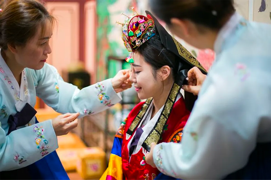 工作人员帮助新娘调整传统婚礼头饰，这是韩国传统婚礼准备的一部分。