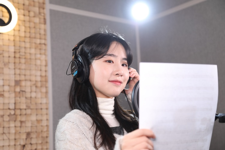韓国ソウルにあるK-POPレコーディングスタジオでのレコーディング体験の一幕。ヘッドフォンを装着し、歌詞を読みながらマイクの前で収録している様子です。