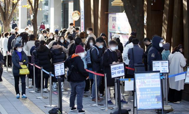 ソウル松坡区保健所の選別診療所の外で、大勢の市民たちが新型コロナウイルス感染症検査を受けるために並んで待っている。COVID-19の確診者数が増加している様子を示す画像。