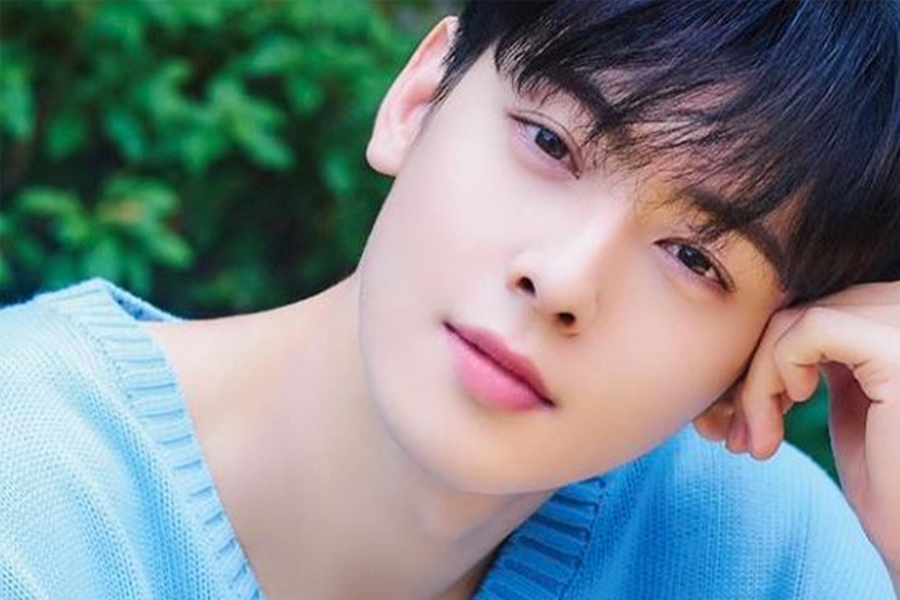 男子面部模糊，身穿淺藍色毛衣，背景為綠色植物。