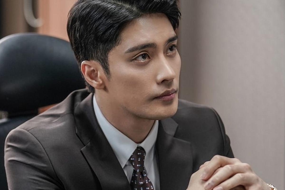 Người đàn ông mặc vest, đang ngồi trong văn phòng với biểu cảm nghiêm túc.