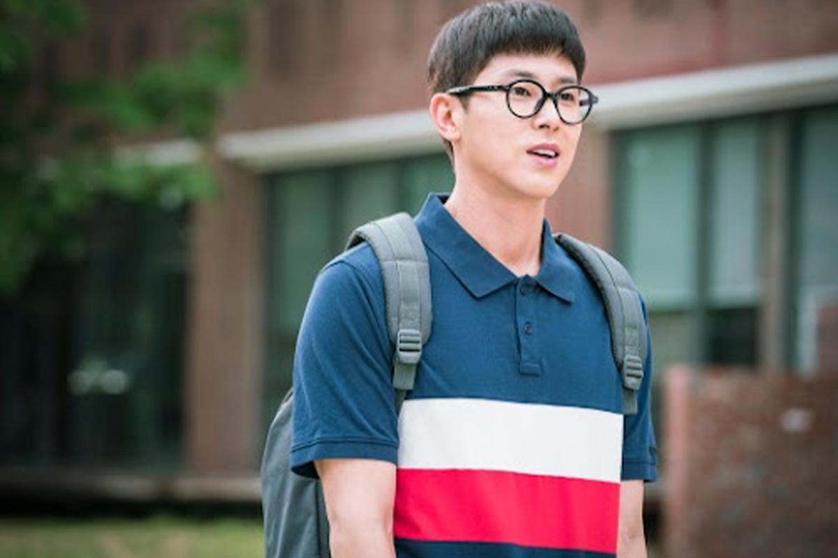 Sinh viên nam trẻ tuổi mặc áo polo và ba lô, đứng trước trường học.