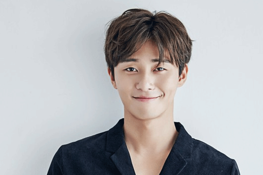 男子面部模糊，身穿黑色服裝，背景為淺灰色牆壁場景。