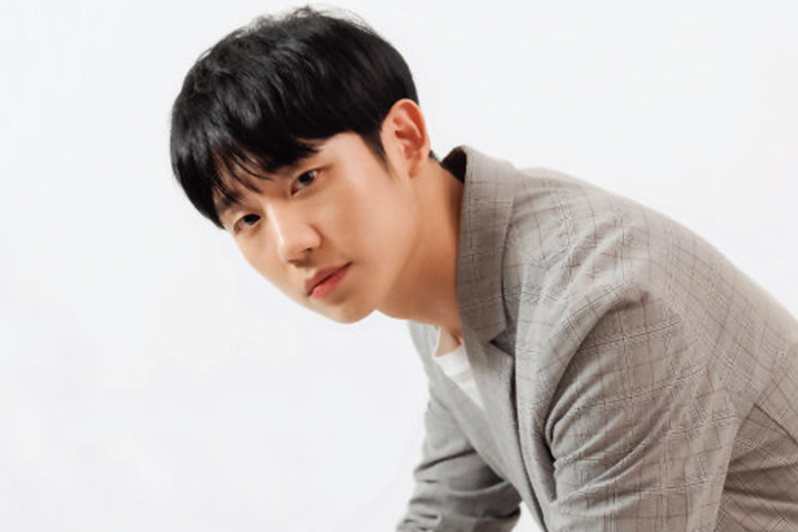 男子身穿灰色格紋西裝夾克，面部模糊，背景為白色。