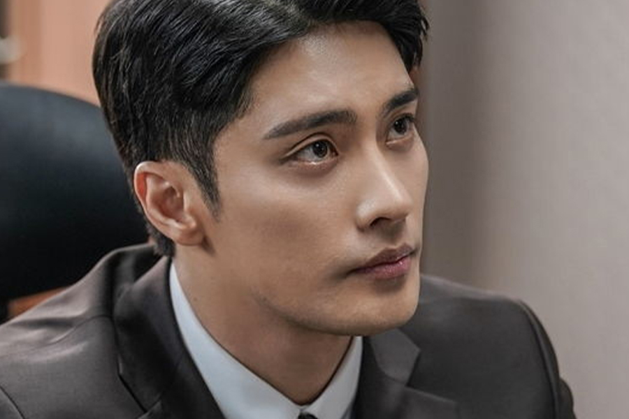 男子臉部模糊，身穿正式西裝坐在辦公椅上，背景含有灰色牆壁。