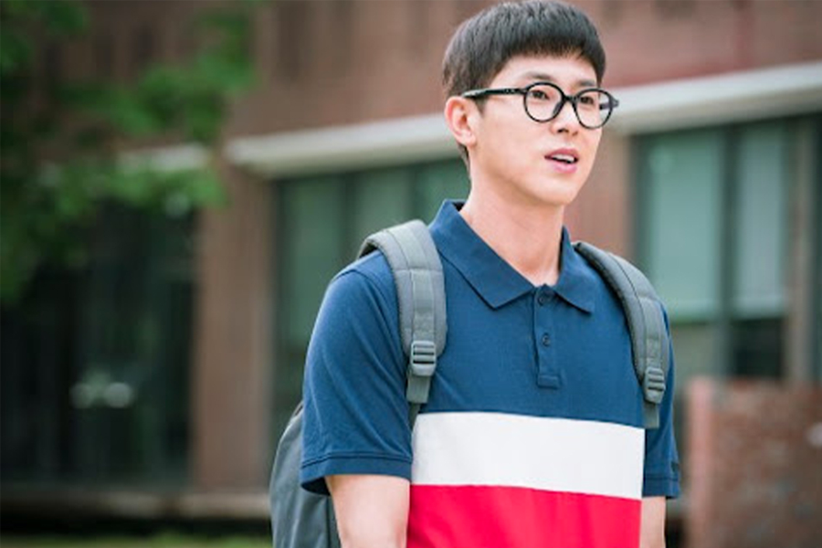 男子面部模糊，身穿深色T恤衫與揹包，背景為淺色建築物。