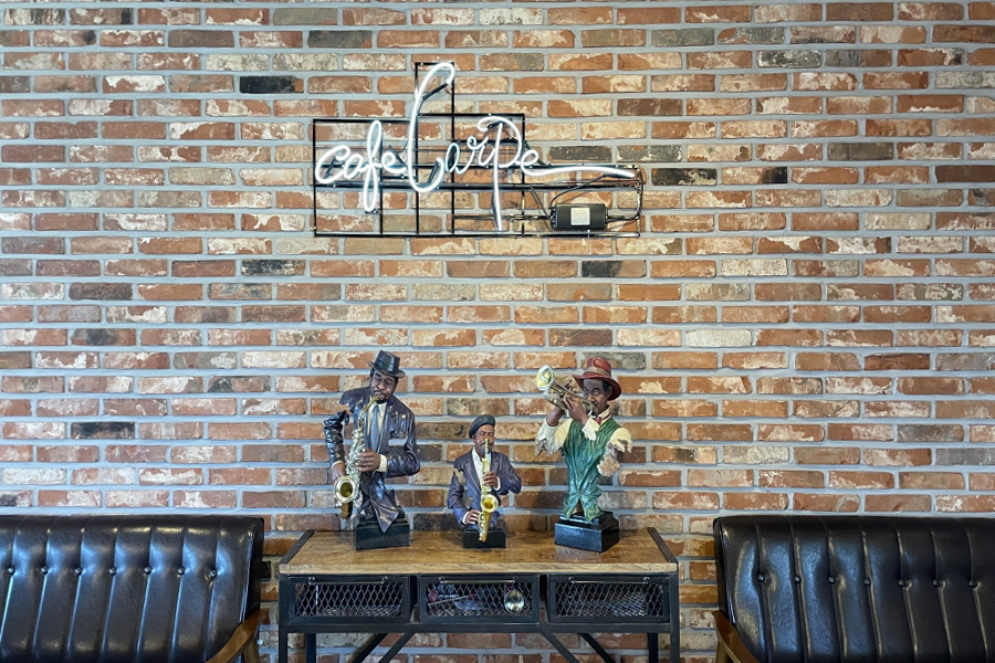磚牆前陳列樂器人物雕像的搖椅區，突顯春川Cafe Carpe的獨特氛圍