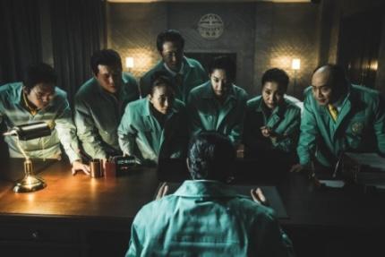 Netflixオリジナル韓国シリーズ「地獄が呼んでいる」のシーン。暗い部屋で、中央の人物を取り囲む者たちが慎重に機を見下ろしている。