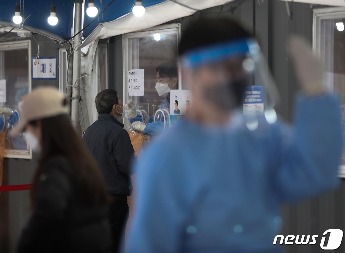 ソウル駅の選別診療所で、新型コロナウイルス検査を受ける市民たち。防護服を着た医療スタッフが検体を採取している様子。