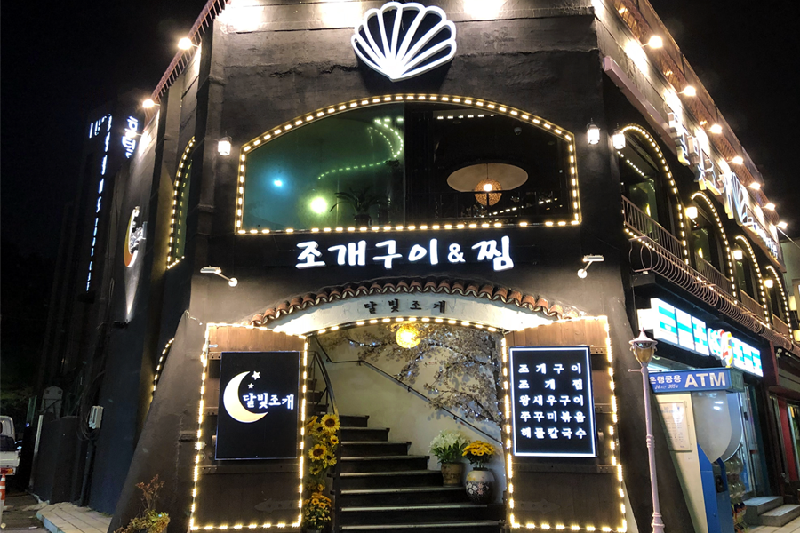 Exterior of Dalbit Shellfish Grill in Wolmido, Incheon, South Korea, illuminated at night with decorative lights.
