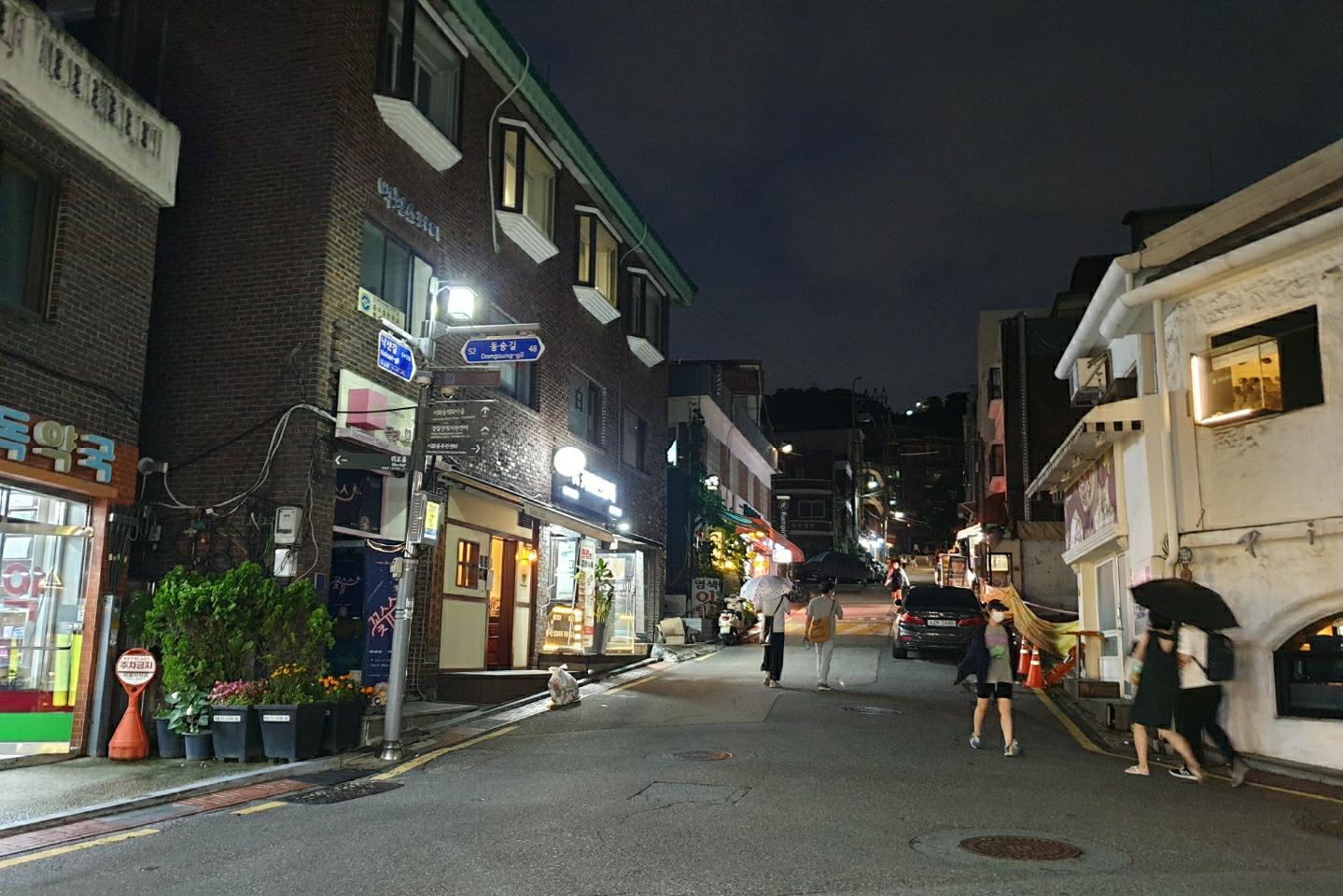 夜間に散歩する人々が行き交うソウルの街並み。古き良き時代を感じさせる建物と共に秋の夜風に吹かれる様子が伺える。