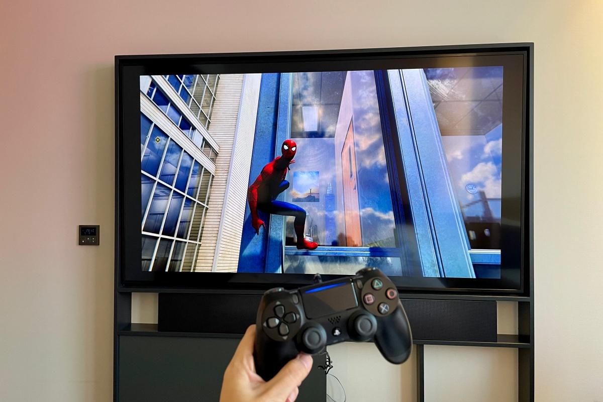 ソウル新羅ステイ三成の客室でプレイステーションを使用する様子。スパイダーマンのゲーム画面が大きなテレビに映し出されており、手にはコントローラーが握られています。高級ホテルのモダンな室内で、ゲームを楽しむための最適な環境を提供しています。