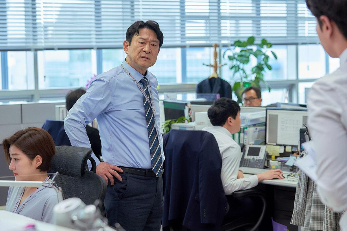 ออฟฟิศที่มีพนักงานนั่งทำงานอยู่ในออฟฟิศองค์กรเกาหลี ซึ่งสะท้อนถึงบรรยากาศที่เกิดขึ้นในที่ทำงานของบริษัทในเกาหลีใต้ โดยมีโต๊ะทำงานและเครื่องใช้สำนักงานอยู่รอบ ๆ แสดงถึงวัฒนธรรมการทำงานในเกาหลีรวมถึงความท้าทายที่เกี่ยวข้องในสภาพแวดล้อมนี้