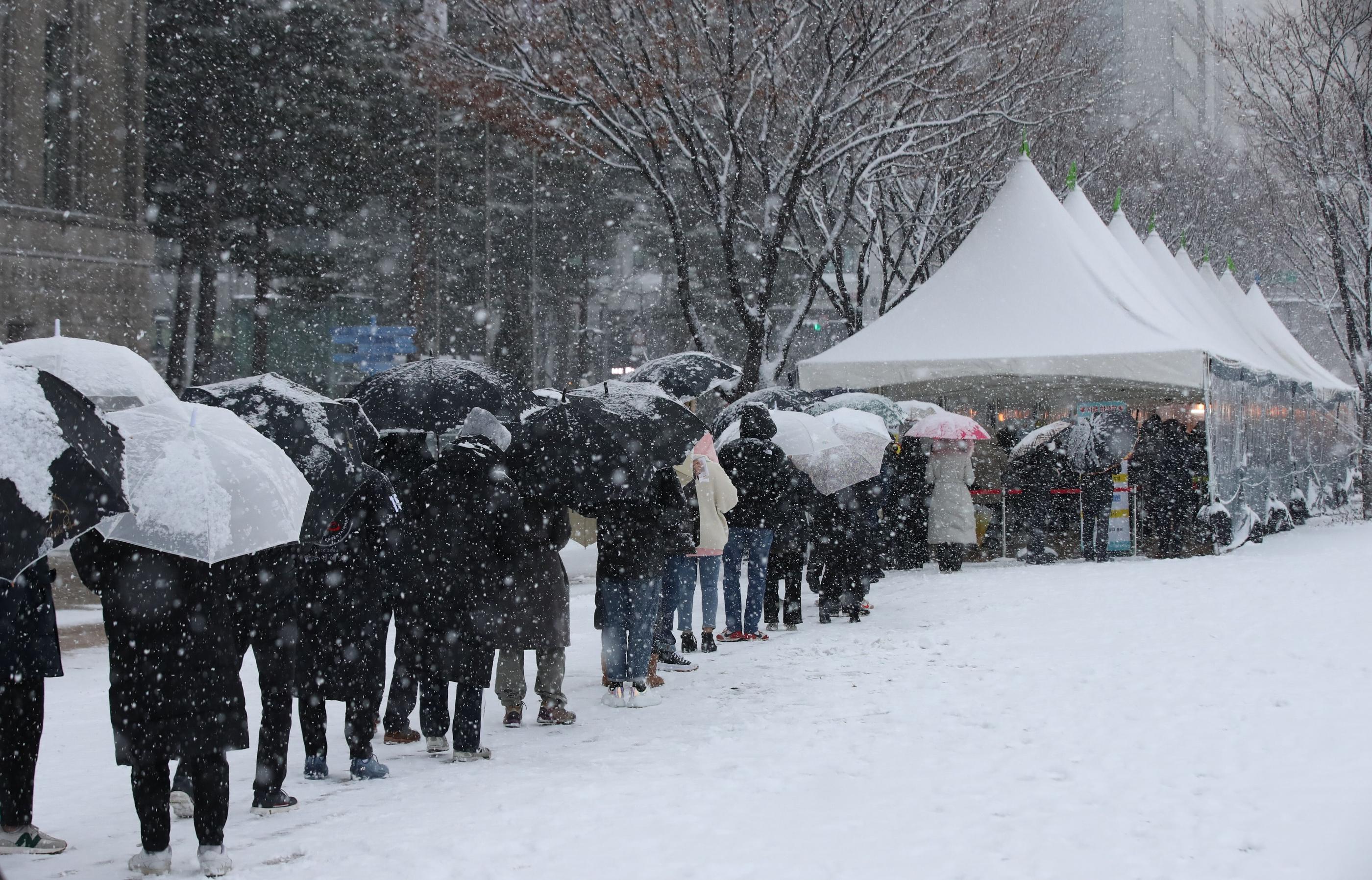 ソウル市庁のコロナ19検査所で、大雪の中で並んでいる市民たちの行列。傘をさしながら待つ姿。