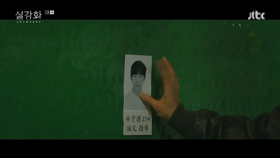 照片顯示一隻手將一張紙條貼在綠色的背景板上，紙條上方是模糊的臉部，圖片來源為韓劇《雪降花》。