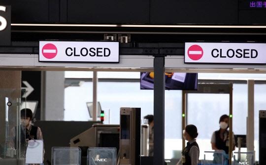 成田国際空港の出入口に「CLOSED」のサインが掲示されている。背景にはマスクを着用した空港職員が勤務中で、日本政府の入国規制を示唆している様子。