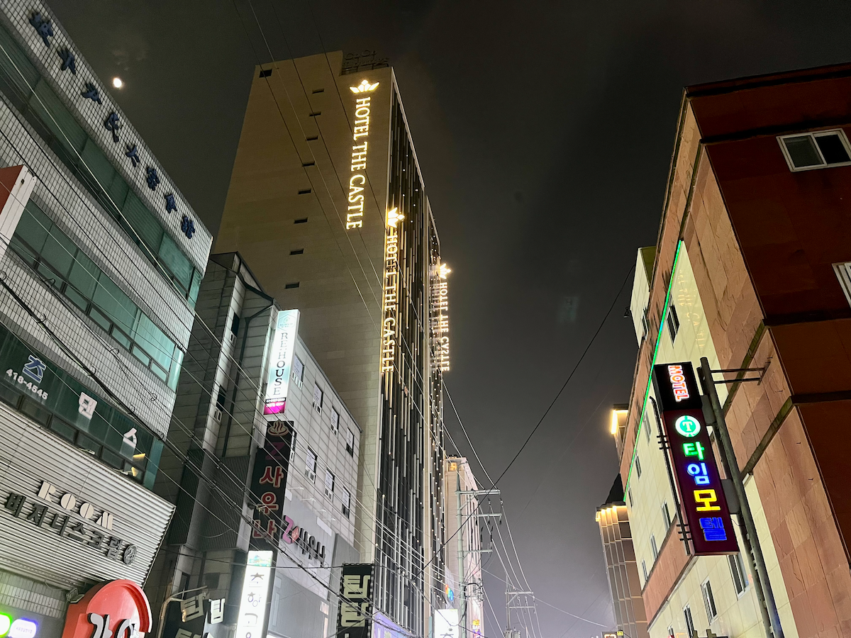 Nachtsicht auf das Hotel The Castle mit beleuchteten Schildern und umliegenden Gebäuden.