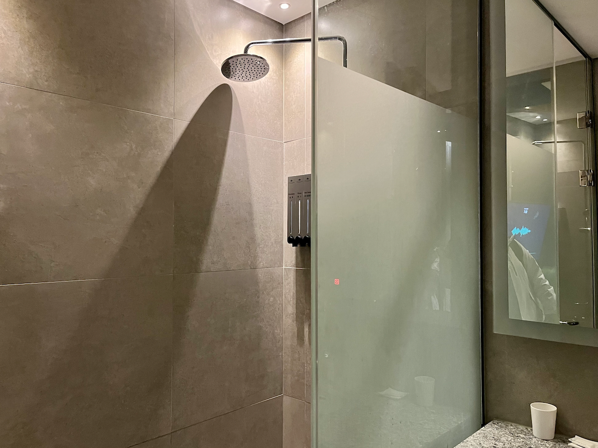 Großzügige Dusche mit beige gefliesten Wänden im Hotelbadezimmer.