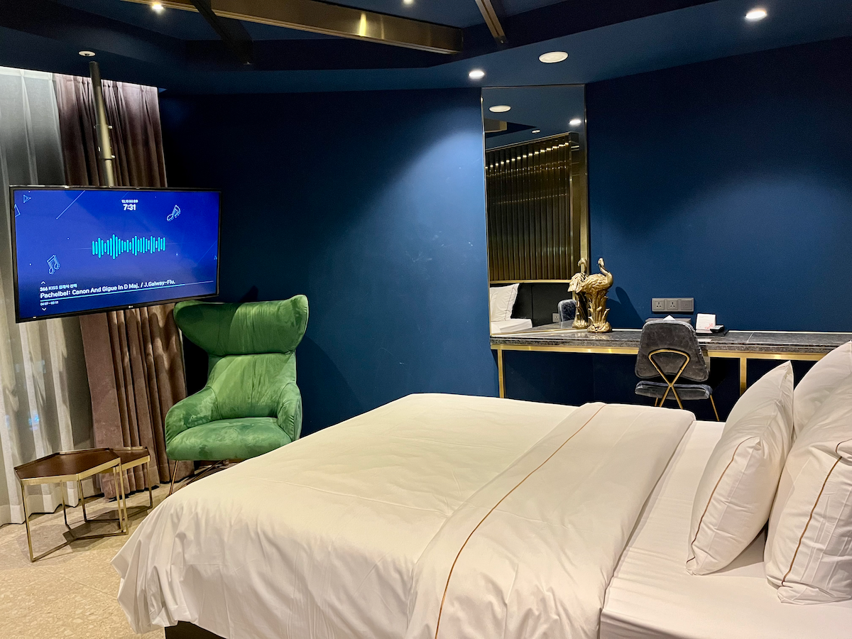 Innenansicht eines eleganten blauen Hotelzimmers mit einem großen Bett und einem Fernseher.