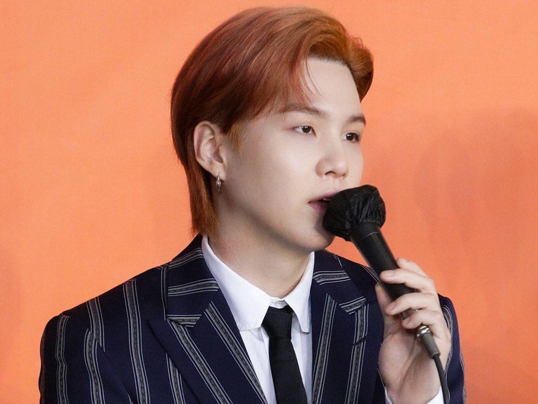 BTSのメンバーSUGAがマイクを持って話している様子。SUGAはグループの一員として有名。