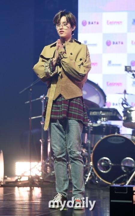 日本のバンドDAY6のメンバーがコンサートで感謝の意を示している様子。腕を組んでマイクを持ち、感謝の気持ちを表現しています。ステージにはドラムセットが配置され、演奏の準備が整っています。