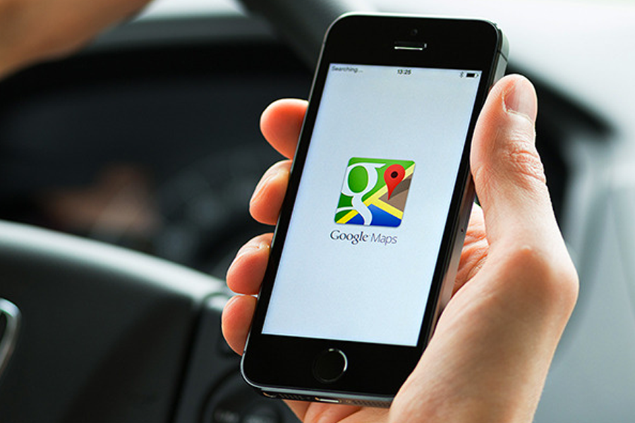 大手の中握著一臺手機，屏幕上顯示Google地圖圖標，道路兩邊模糊的背景中可看到一些樹木。