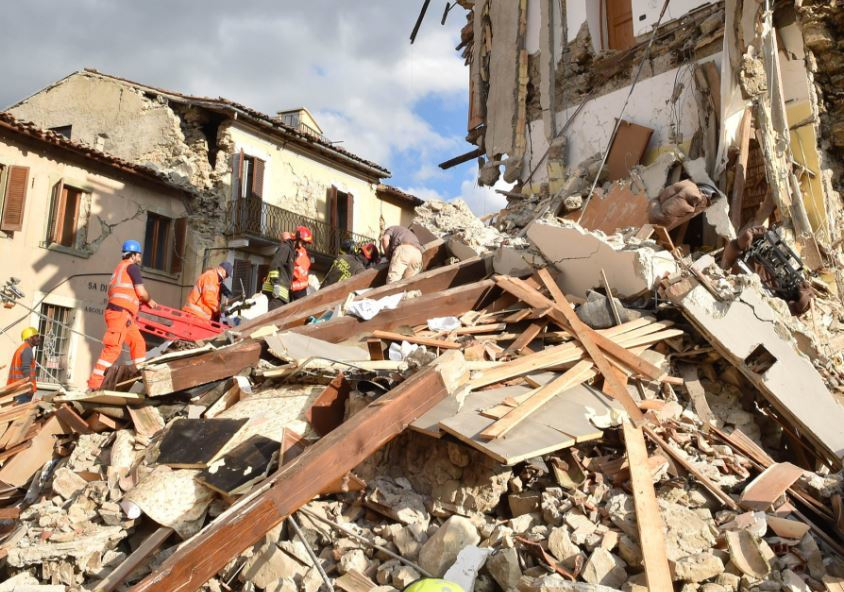 地震後倒塌建築的搜救場景，救援人員在瓦礫堆中進行搜索和救援，背景為嚴重損毀的建築物。