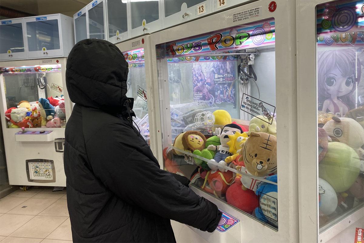Person engaged in playing with a claw machine, trying to win soft toy plushies in Seoul's prize arcade