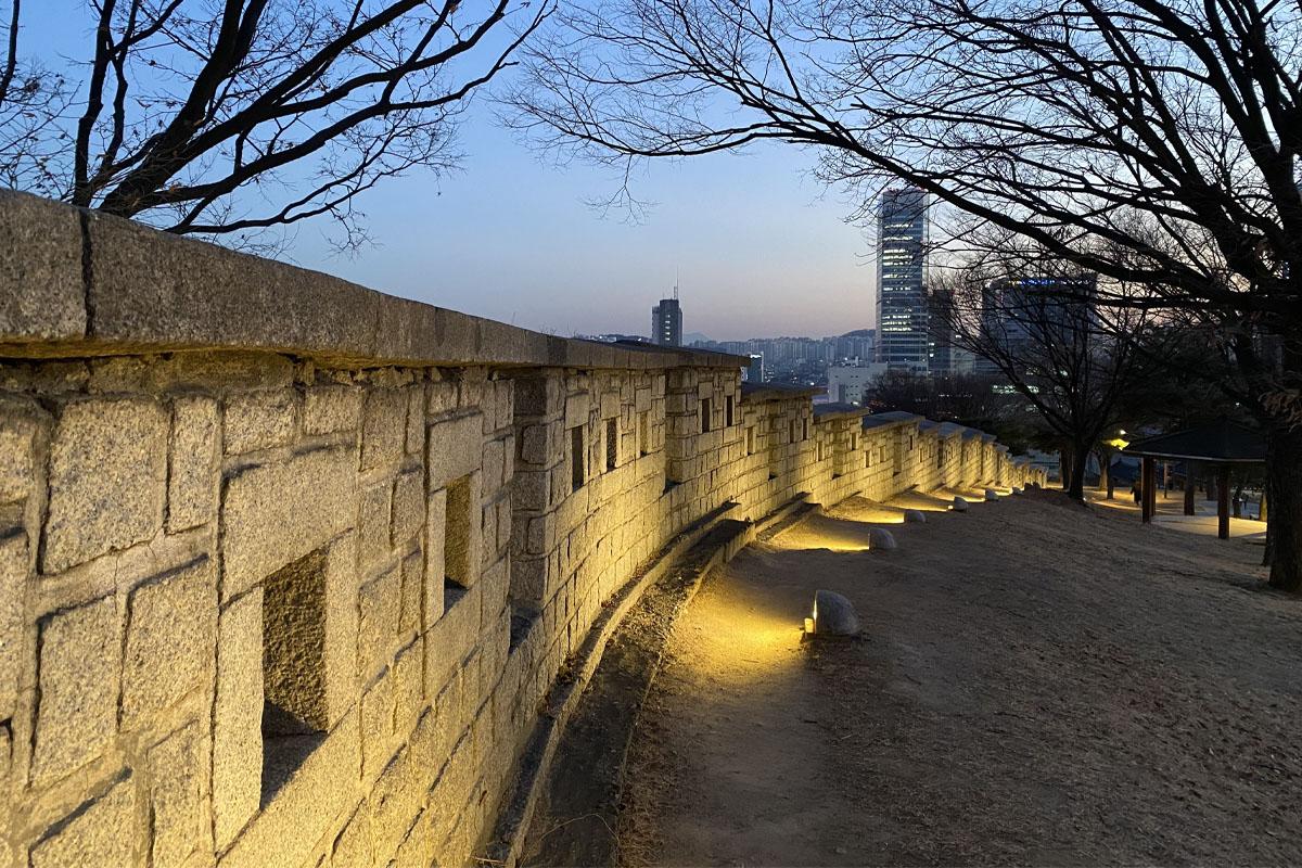 Historic stone wall featured at Heunginjimun Park in Seoul lit up at night, with cityscape in the background