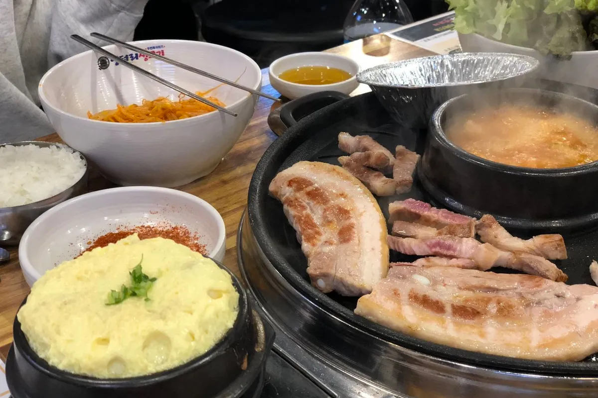 韓國烤肉店的桌面上擺放著各種菜品，包括煎蛋、泡菜、米飯和燒烤肉類，以及熱騰騰的湯。