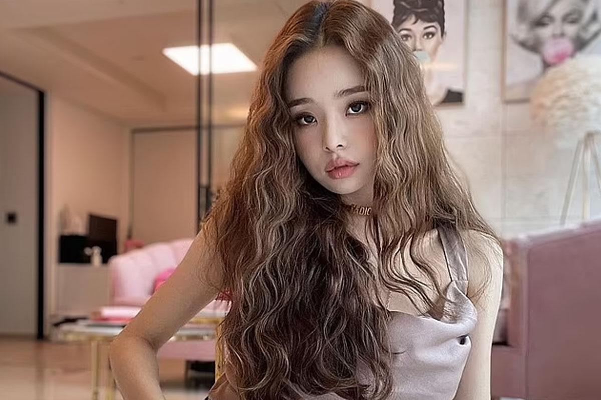 ซงจีอาสวมชุดสีเทายาว มีผมยาวและหยักสวยงามในห้องนั่งเล่นที่มีโทนสีชมพูอ่อนและสีเบจ