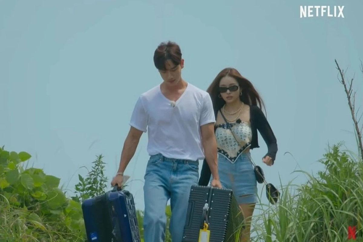 คู่จิ้นจากรายการ Singles Inferno ซงจีอาและคิมฮยอนจุงเดินถือกระเป๋าเดินทางบนเกาะในรายการทีวีของ Netflix