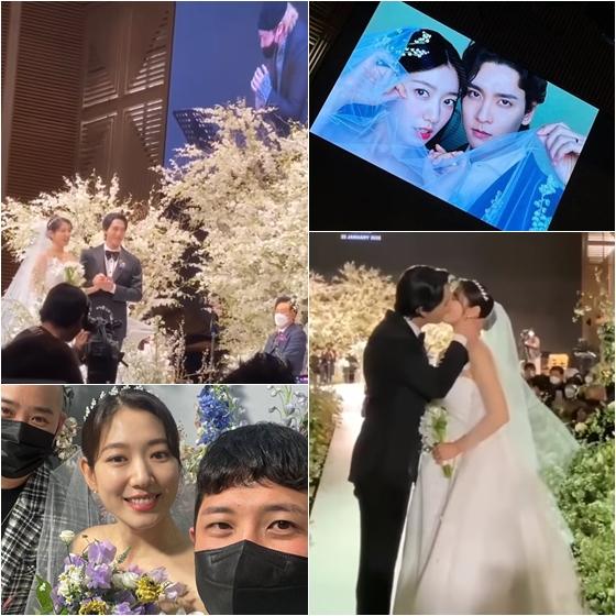 パク・シネとチェ・テジュンの結婚式の写真。新郎新婦が神父の前で指輪交換をしている様子です。背景には美しく飾られた白い花々が見えます。