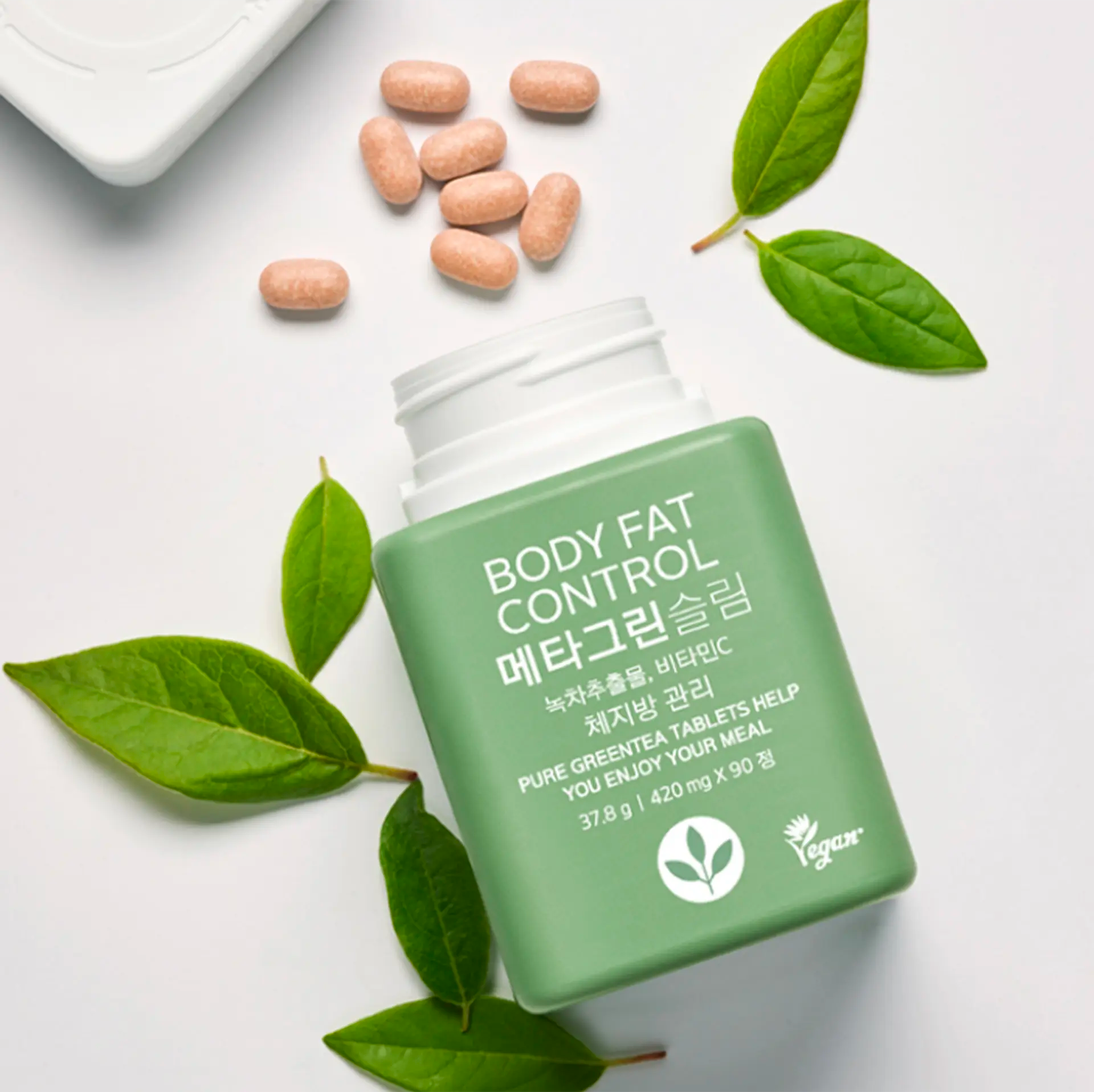 Vital Beautie Meta Green Slim tablets with fresh green tea leaves, promoting vegan-friendly attributes.