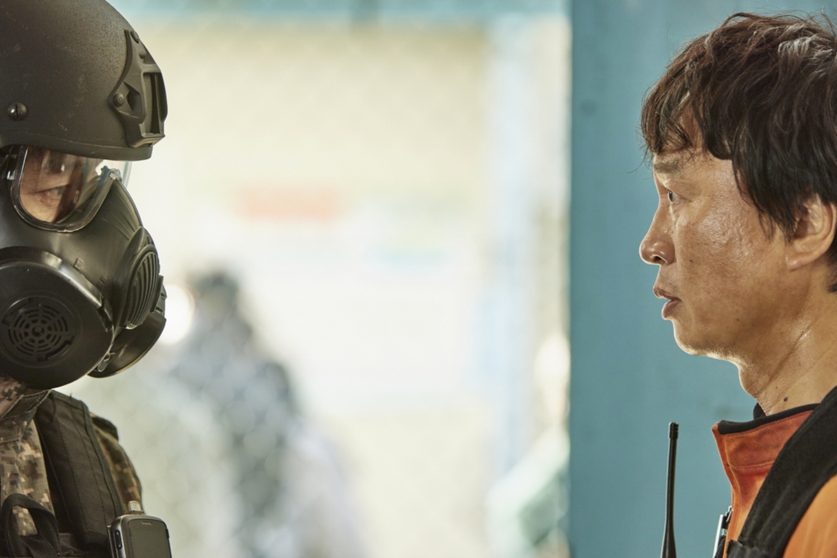 穿著防毒面具的軍人與另一個角色在網狀圍籬前的對話場景，來自Netflix韓劇《殭屍校園》。