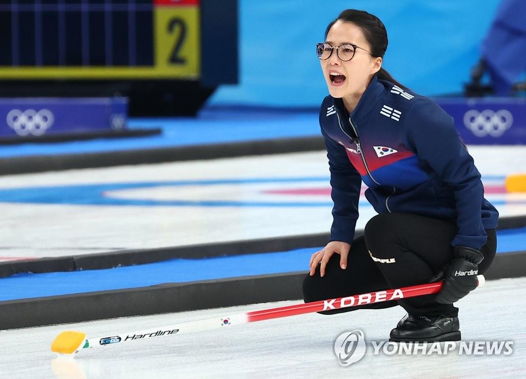 韓国カーリング代表チームの選手が試閤中のオリンピックシーン。韓国のロゴが入った選手用ユニフォームを着用し、カーリングストーンを慎重に観察する姿。