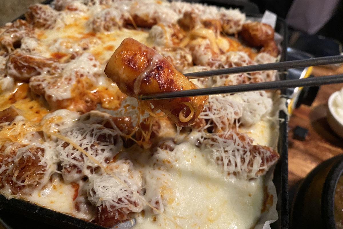 弘大飽肚烤腸的起司脆米腸，筷子夾起一片，起司香氣四溢。