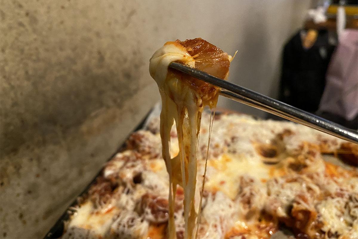 弘대飽肚烤腸中一片牽絲起司包裹的烤腸，使用筷子夾起。