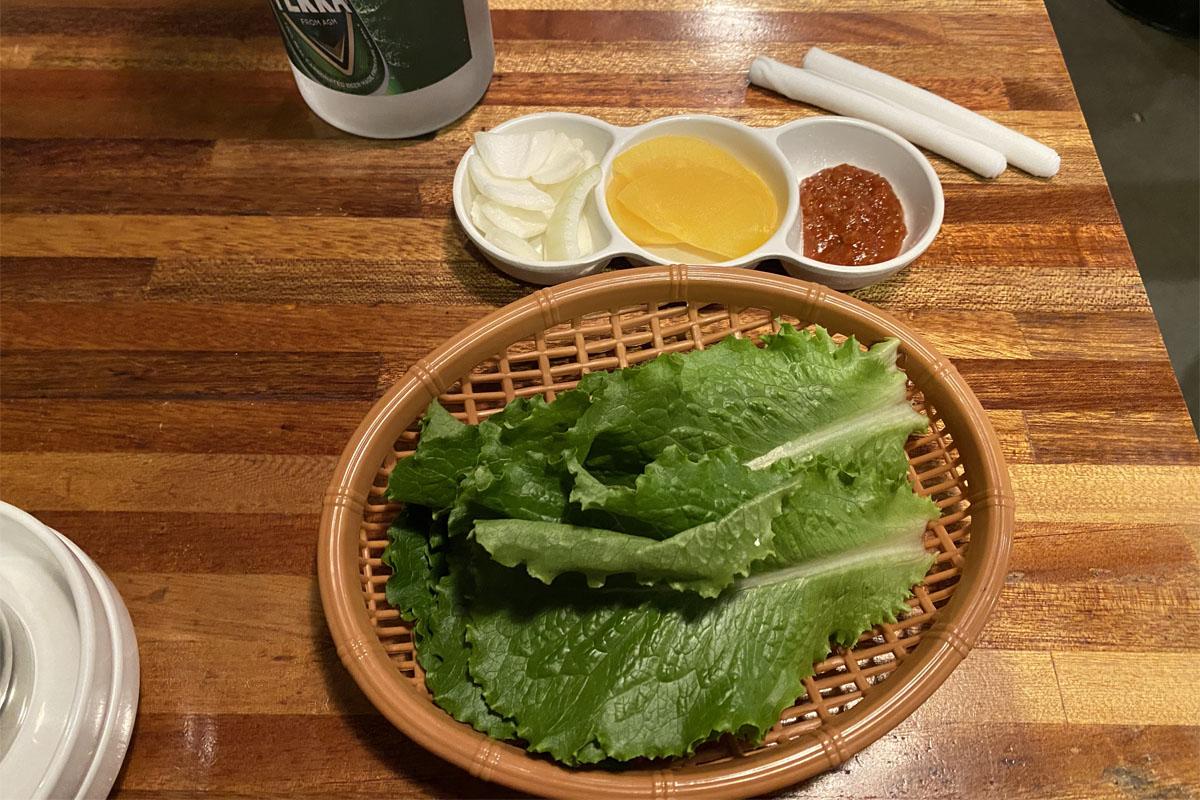 弘대飽肚烤腸提供的小菜，包括生菜、洋蔥、醃製蘿蔔及醬料。